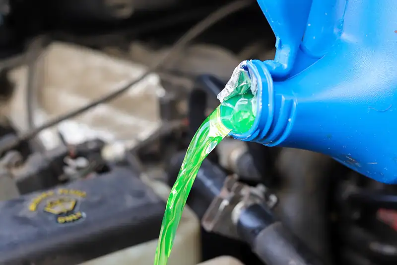 Antivries wordt gegoten vanuit een fles in het koelsysteem van een auto.