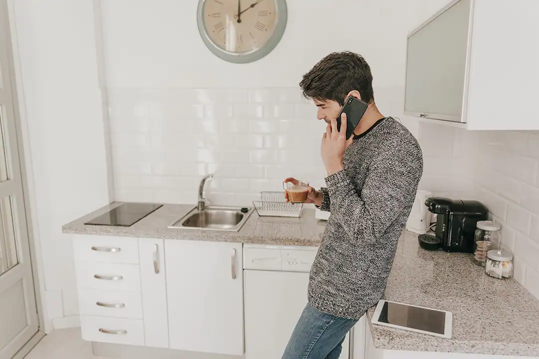 Man in een keuken die een loodgieter belt omdat de gootsteen verstopt is.